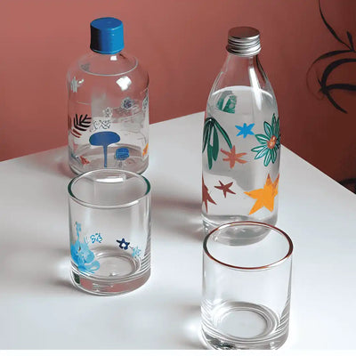 Four clear glass bottles and tumblers with colorful designs.