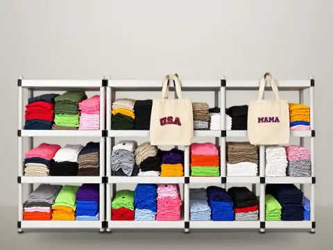 Blank t-shirts stacked by color with two printed canvas tote bags